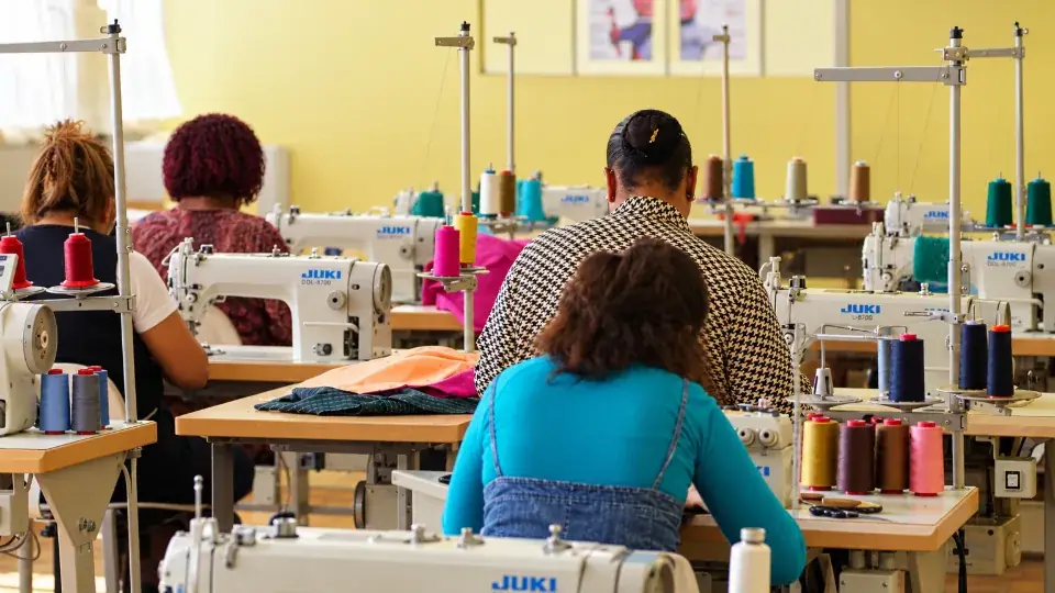 Une main pose un patron en papier sur plusieurs couches de tissu imprimé de fleurs roses et turquoise, avant la découpe.