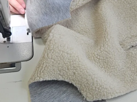 Des mains guident sous le pied de biche un tissu noir rayé de fils dorés.