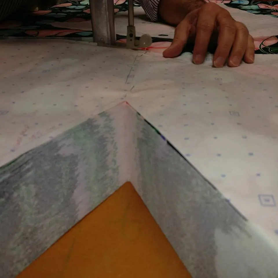 Encolure en V découpée à travers un matelas de tissus superposés, sous le patron en papier pointé.