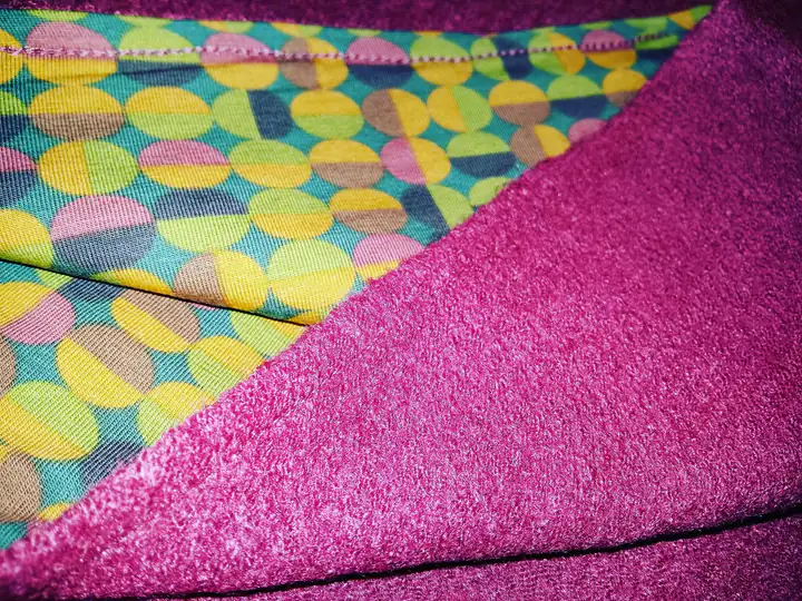 Detail van een kussen in fuchsia badstof, gevoerd met een stof met kleurrijke geometrische motieven.