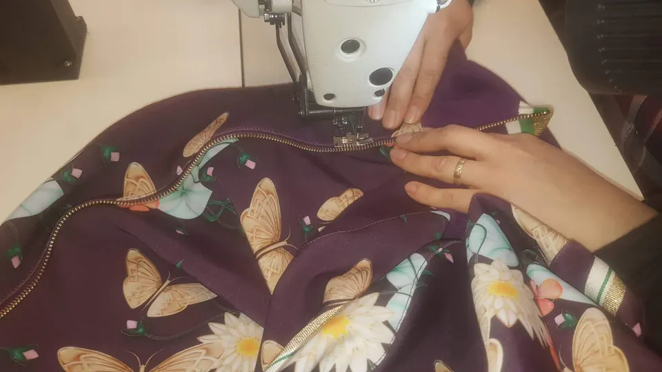 Pose d’une fermeture à glissière dorée sur un blouson violet imprimé de papillons, à la machine industrielle.