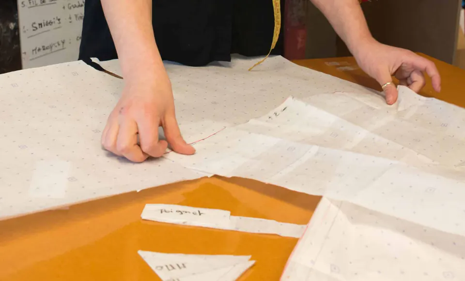 Des mains ajustent des patrons en papier pointé sur la table de coupe.