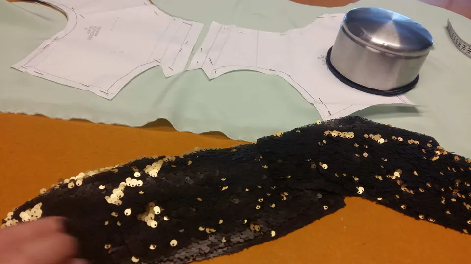 Patrons en papier posés sur un tissu vert d’eau, à côté d’un tissu à sequins noirs et dorés, pour un prototype.