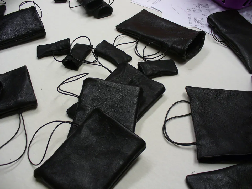 Série de pochettes en simili-cuir noir à cordon, étalées sur une table de l’atelier.